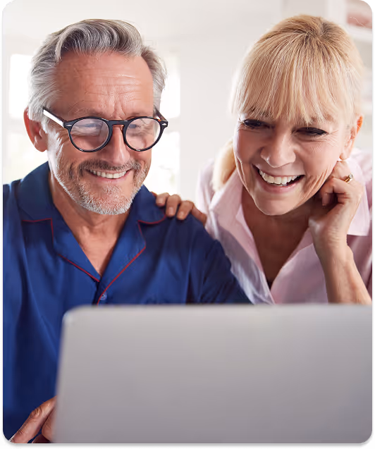 Smiling elderly couple looking at a laptop screen together in a bright room.