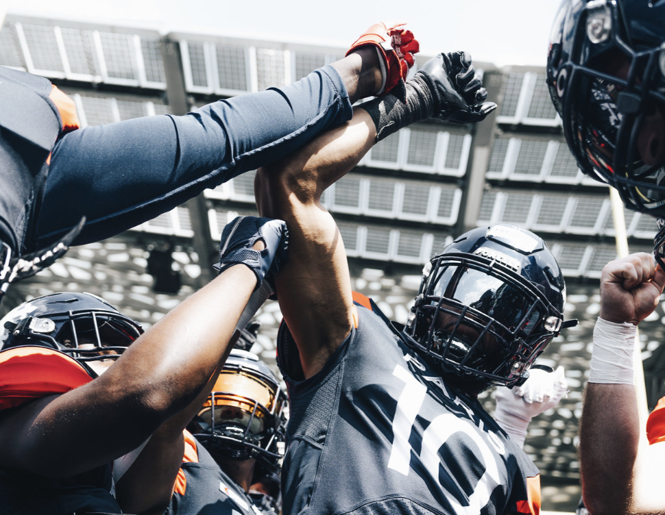 American football players wearing helmets and jerseys celebrating with raised arms under stadium lights.