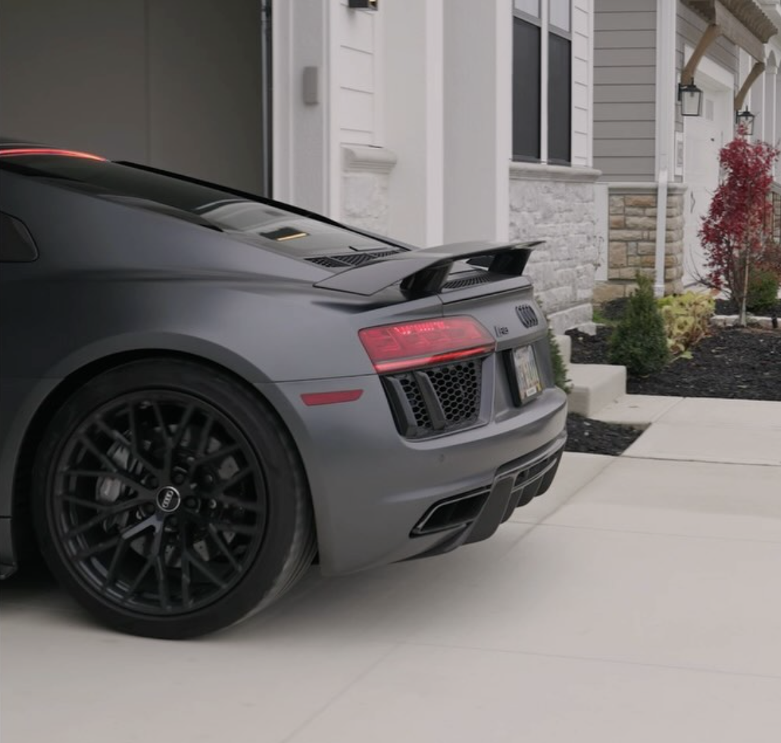 Rear side view of a gray Audi R8 parked in a driveway next to a house.