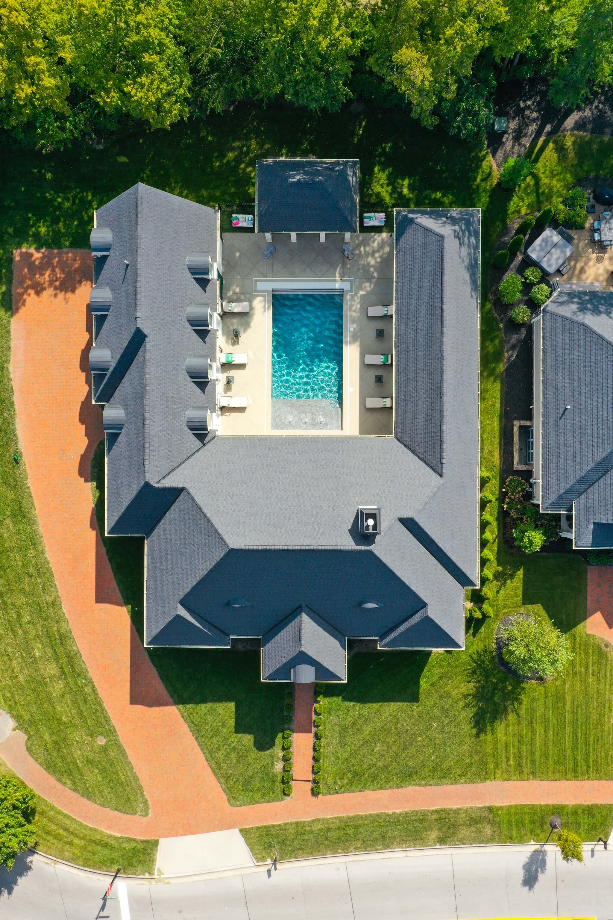 Aerial view of a large U-shaped house with a central swimming pool in the backyard surrounded by lounge chairs and greenery.
