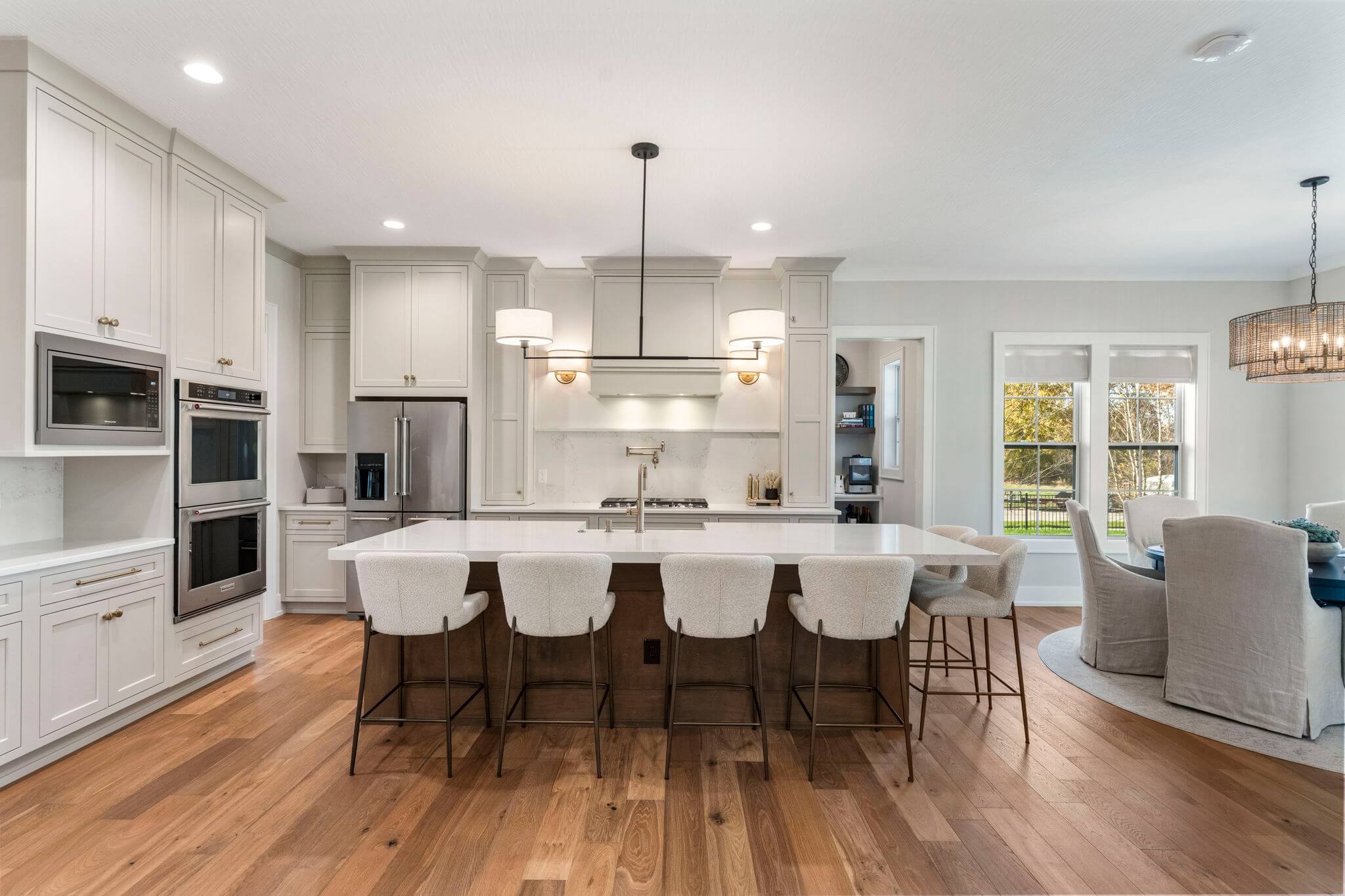 Modern kitchen with white cabinetry, large island with six upholstered bar stools, stainless steel appliances, and hardwood floors.
