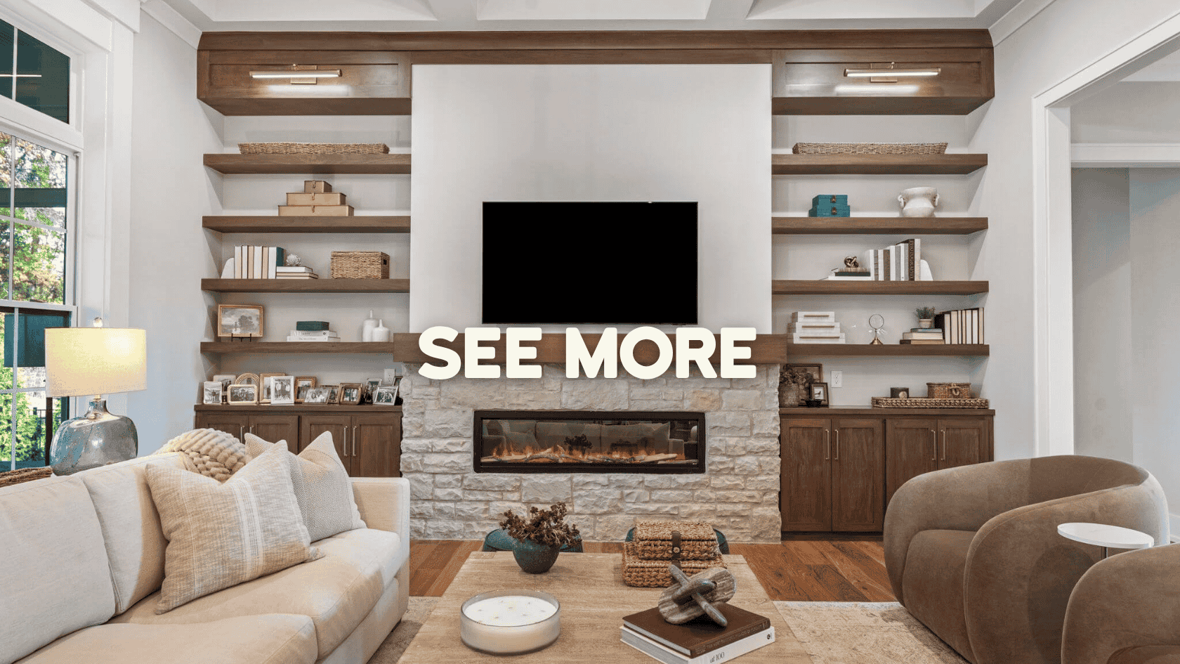 Modern living room with beige sofa, brown armchair, wooden shelves, a stone fireplace, and a TV mounted above, with text 'SEE MORE' overlayed.