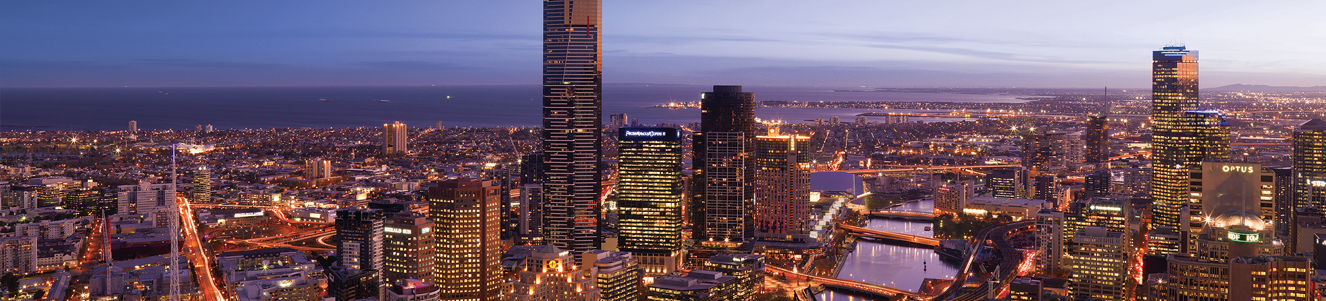Panoramic cityscape of Melbourne at dusk with illuminated skyscrapers and Yarra River.