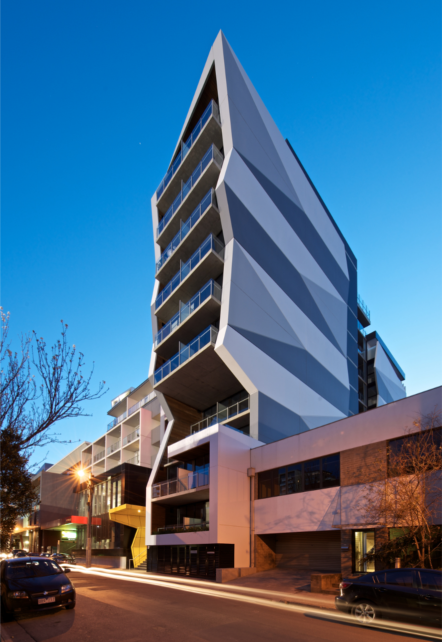Modern angular multi-story building with balconies on a city street at dusk.