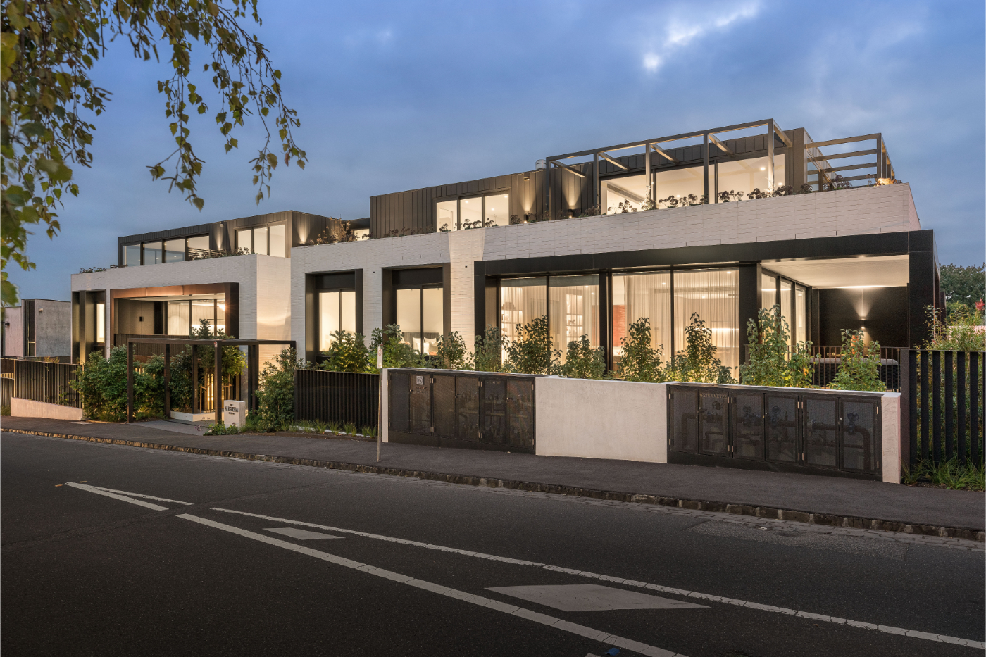 Modern two-story house with large glass windows and a garden in front under a cloudy evening sky.