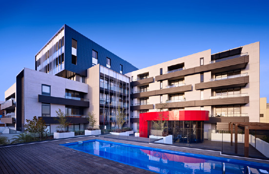 Modern indoor patio with seating area featuring beige chairs with blue pillows, a sectional sofa, marble coffee table, and sliding glass doors overlooking trees.