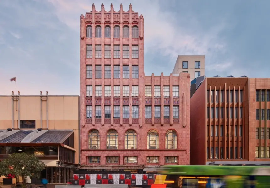 Modern home office corner with marble desk, dark chair, wooden shelves filled with books and decor, and a view of a living room with artwork and a sofa.
