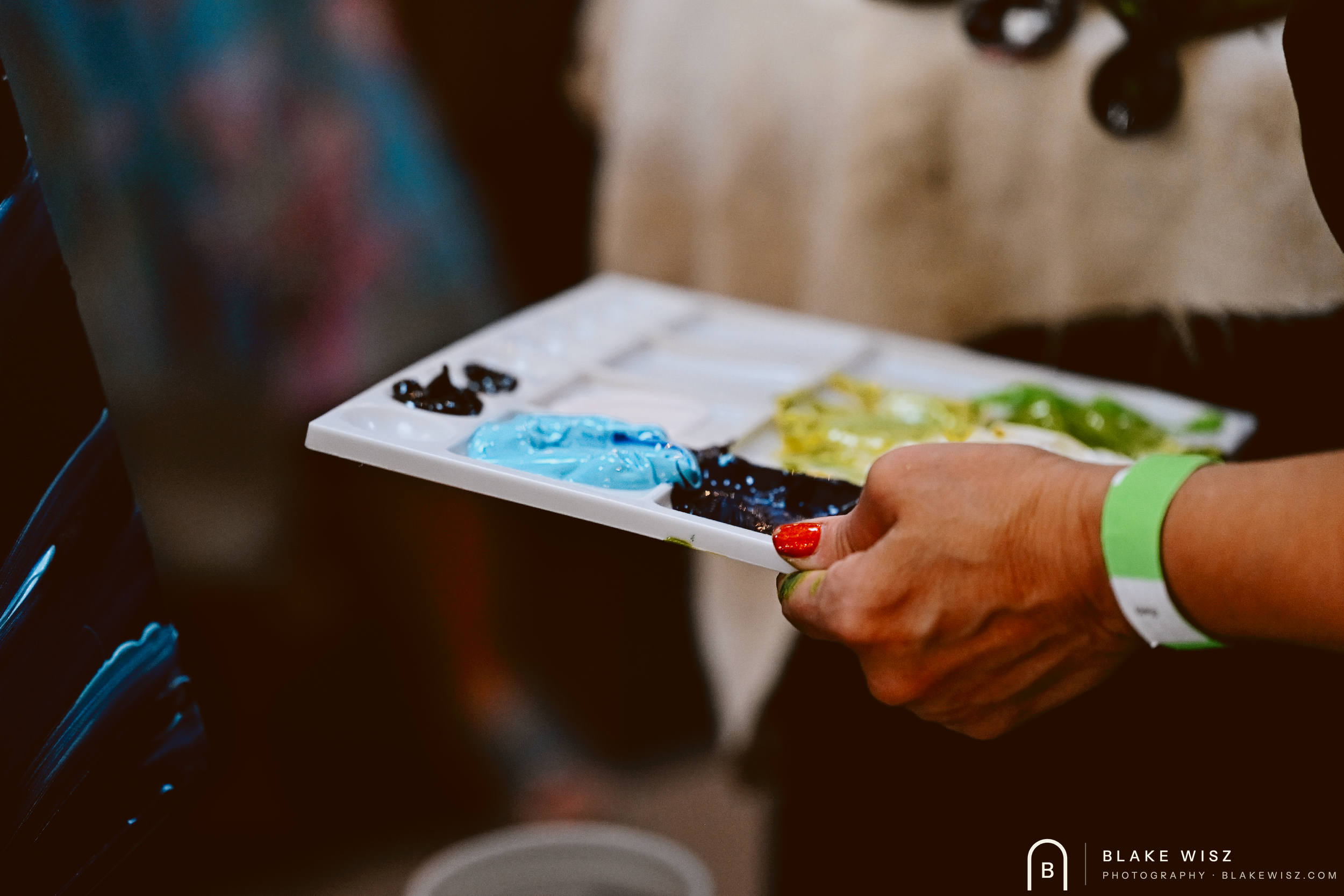 Artist holding a white palette of blue, yellow and green acrylic with a green event wristband