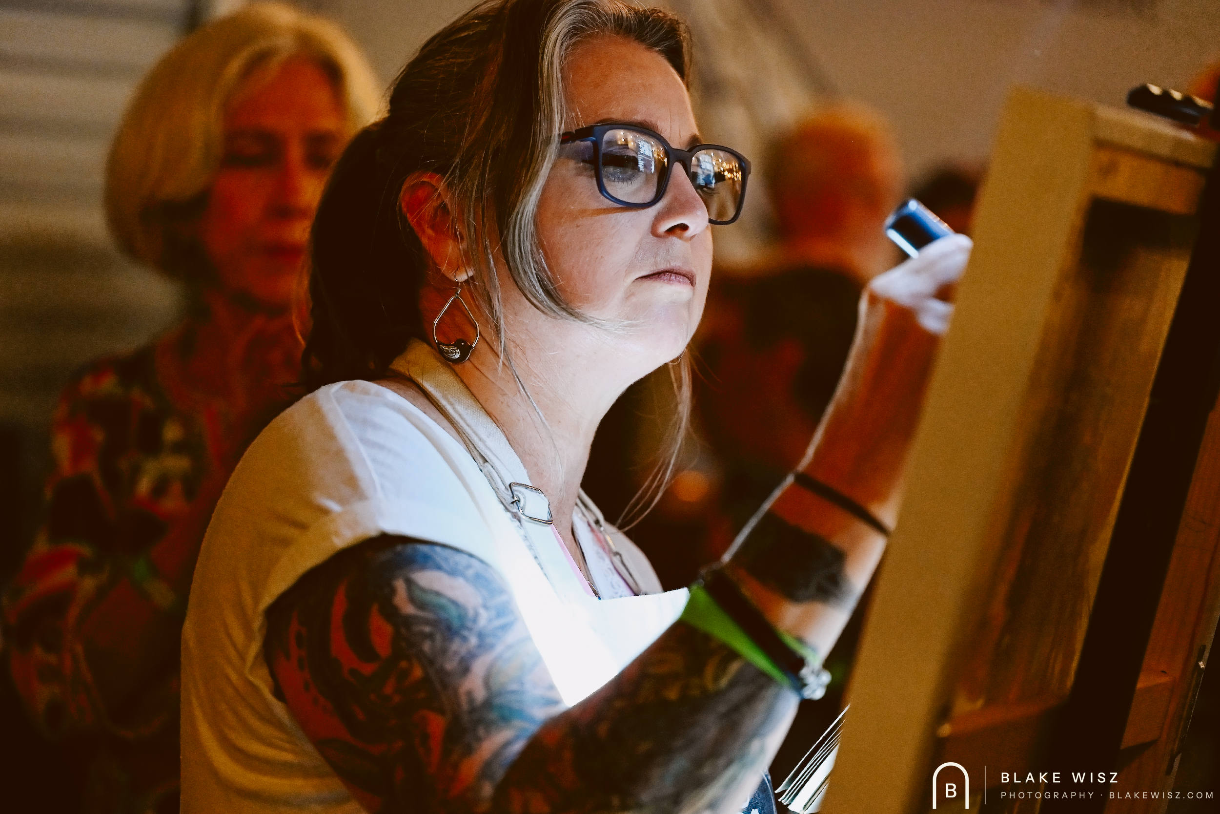 Tattooed artist in glasses painting at her easel at Art Battle Ormond Beach 2026