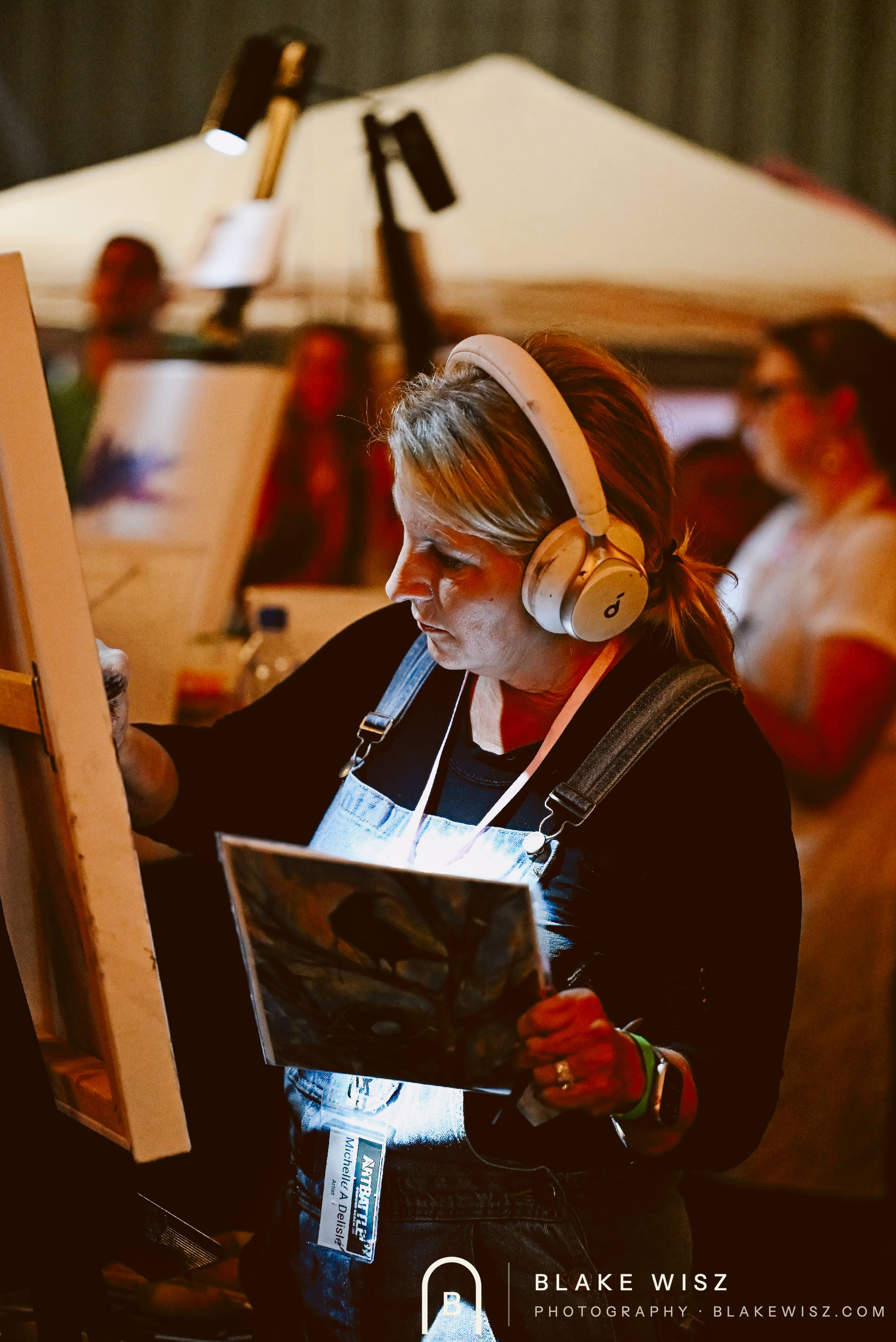 Michelle A Delisle painting in headphones while holding a printed bird reference photo
