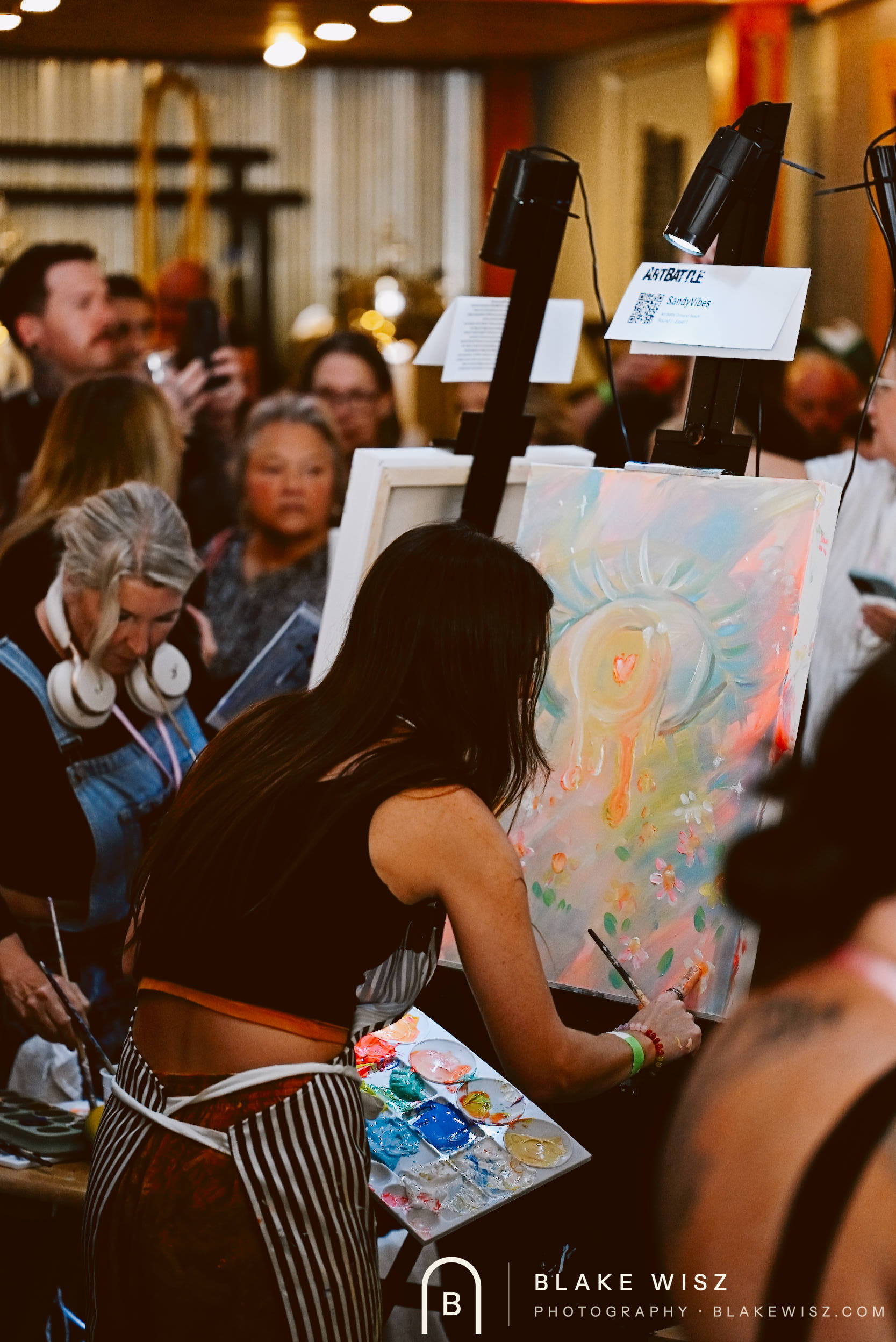 Artist painting a glowing sun motif while the crowd presses in around her easel