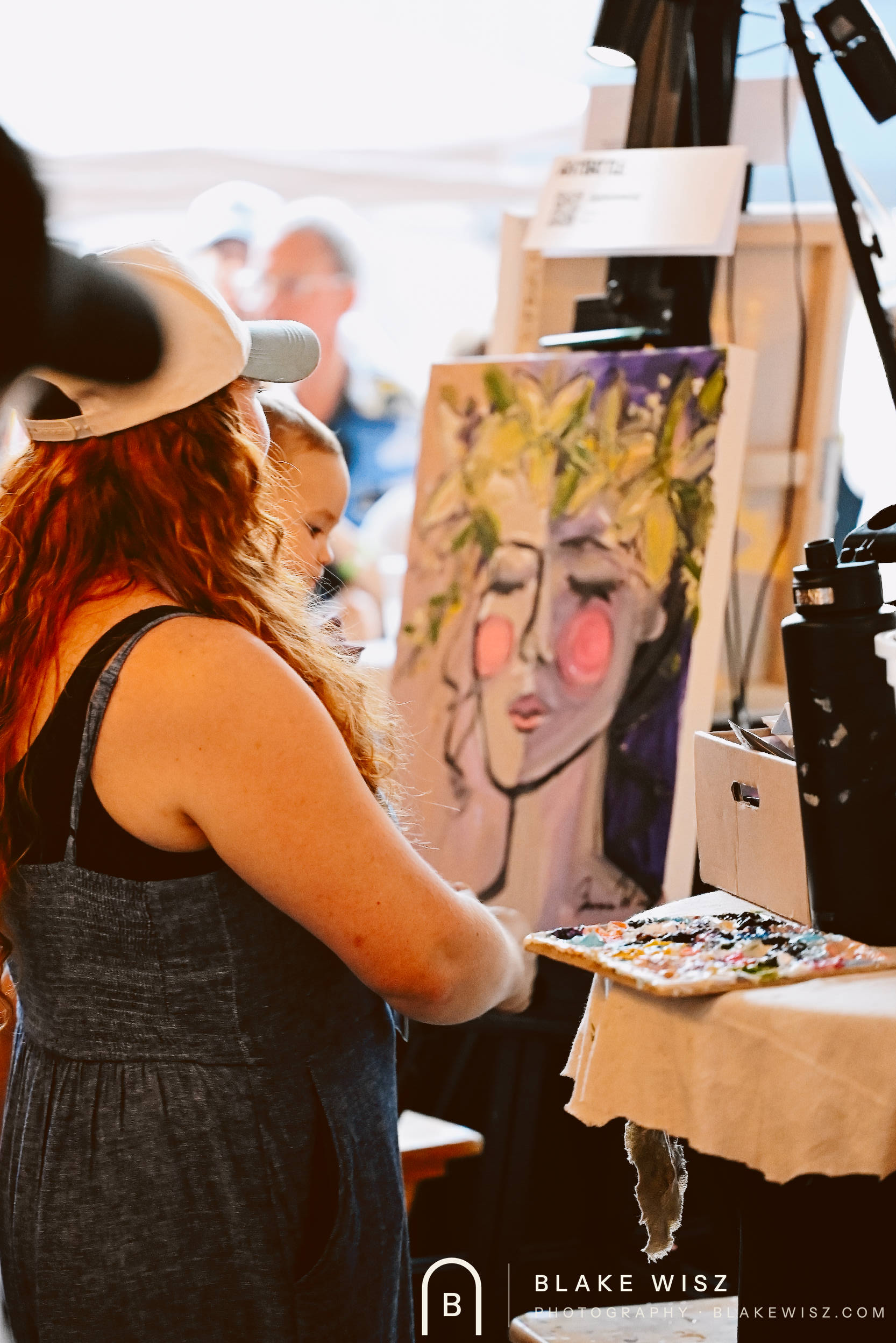 Jasmine Wisz beside her finished portrait holding her palette, Art Battle Ormond Beach
