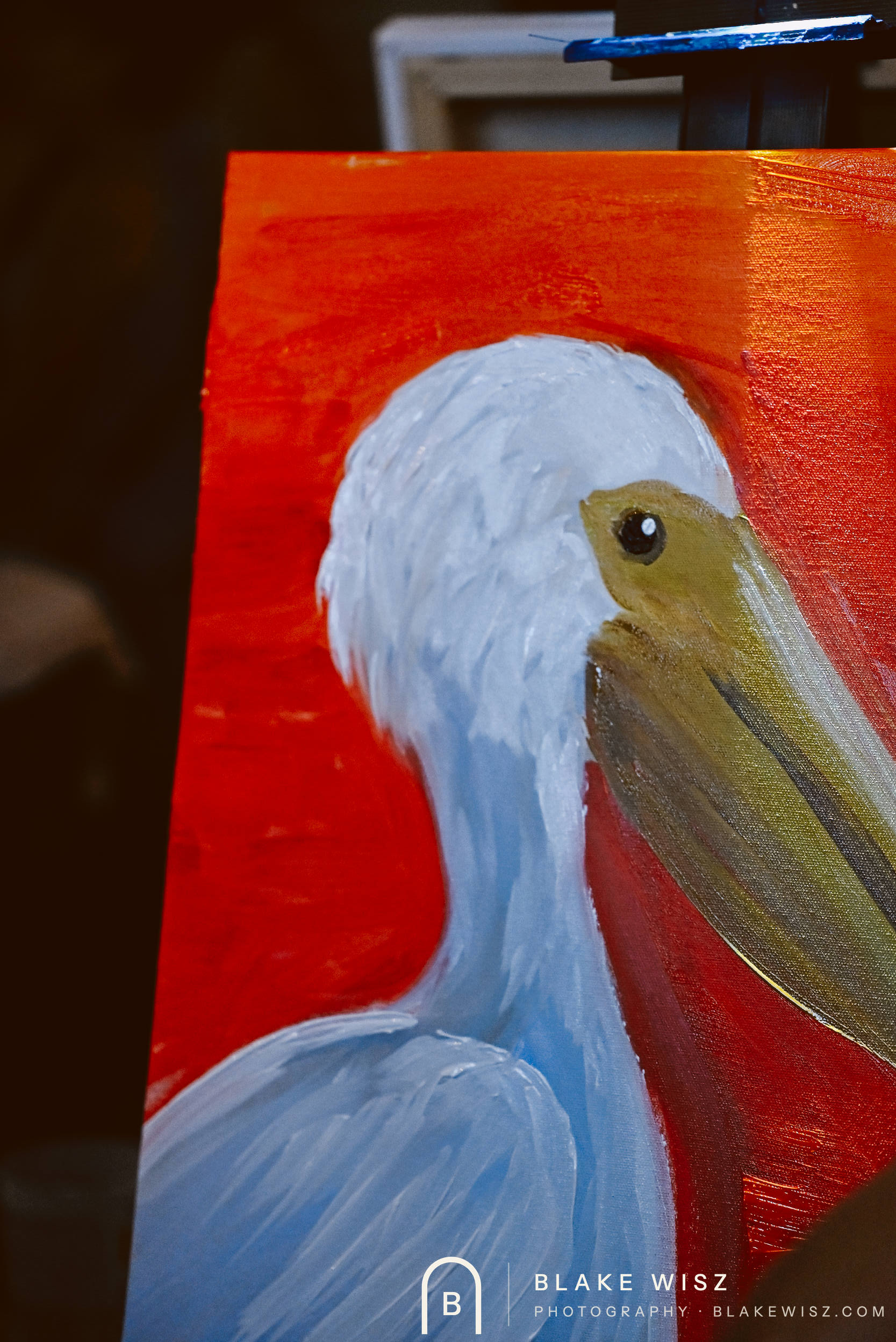 Finished pelican painting in white and gold against a red background on its easel