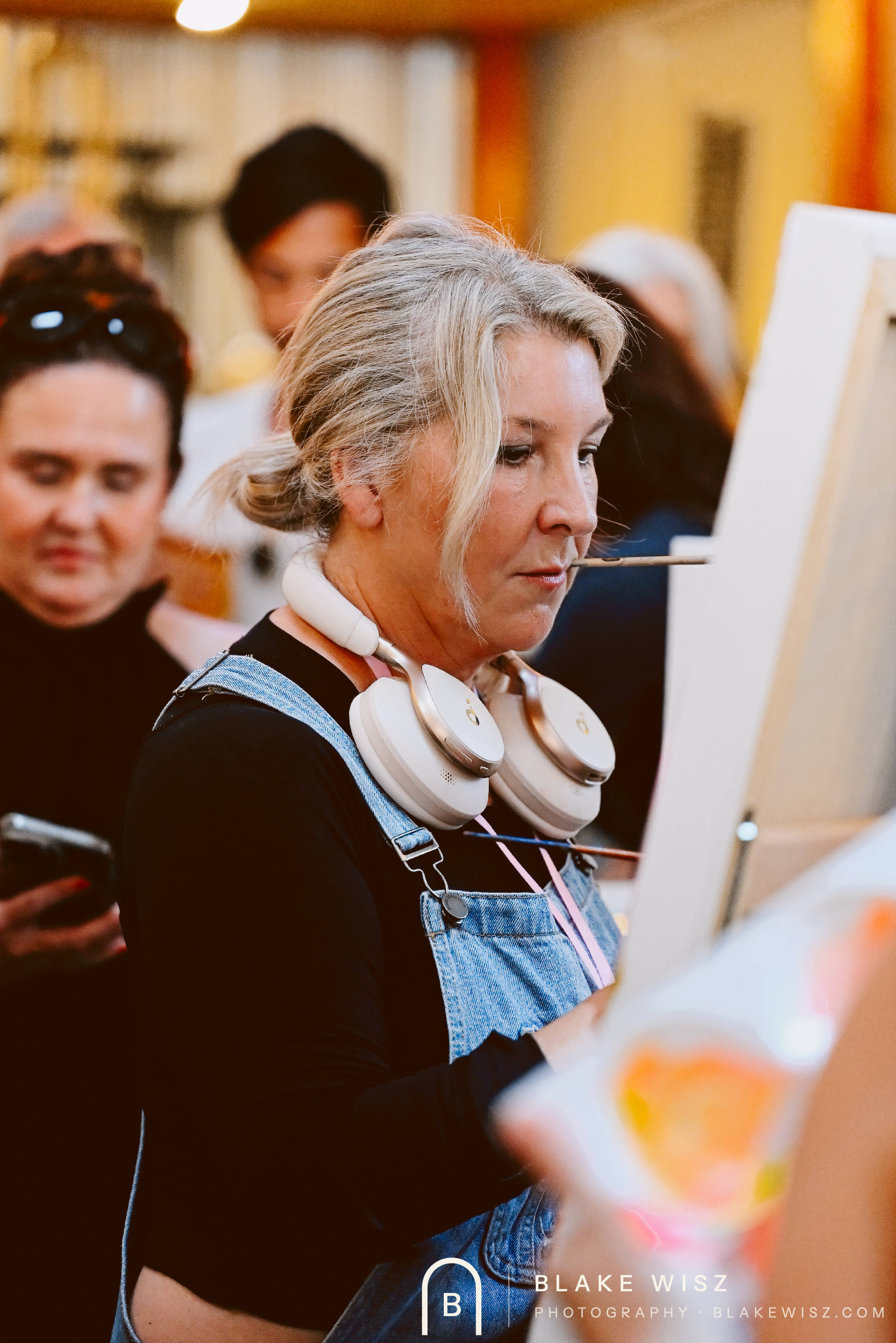 Michelle A Delisle painting with a brush held in her teeth and headphones around her neck