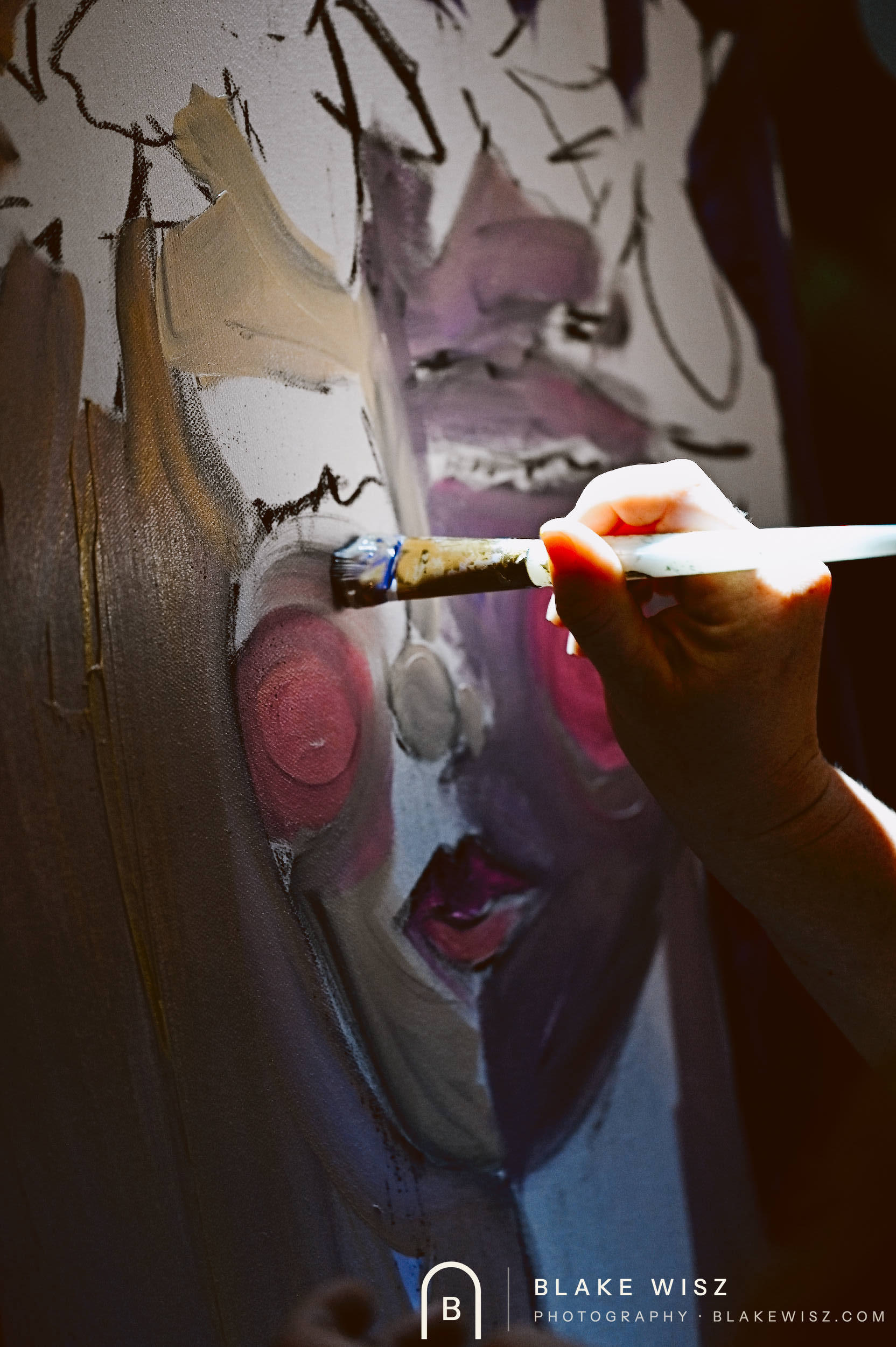 Close-up of a brush laying grey and violet paint into a portrait's face on canvas