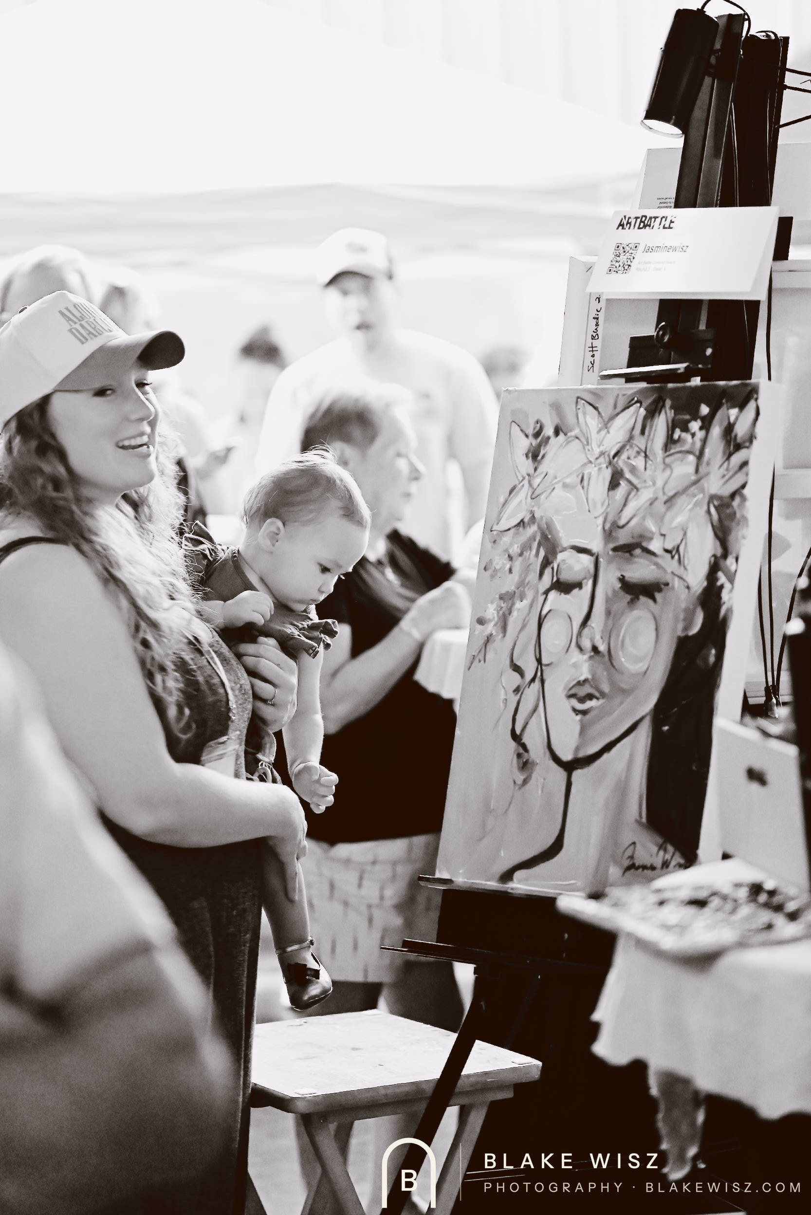 Black and white photo of Jasmine Wisz holding a small child beside her finished canvas