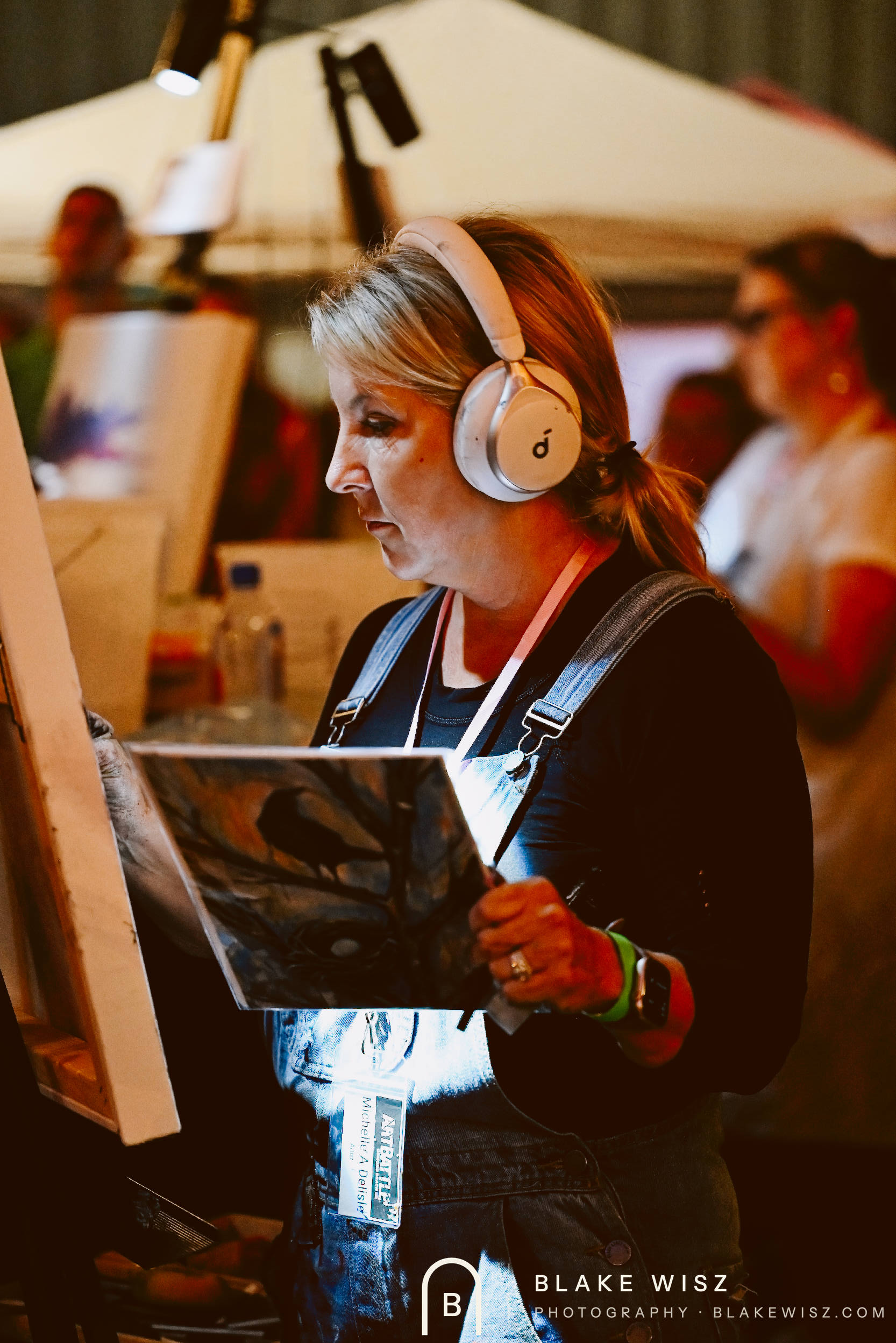 Michelle A Delisle in denim overalls and headphones working from a photo reference