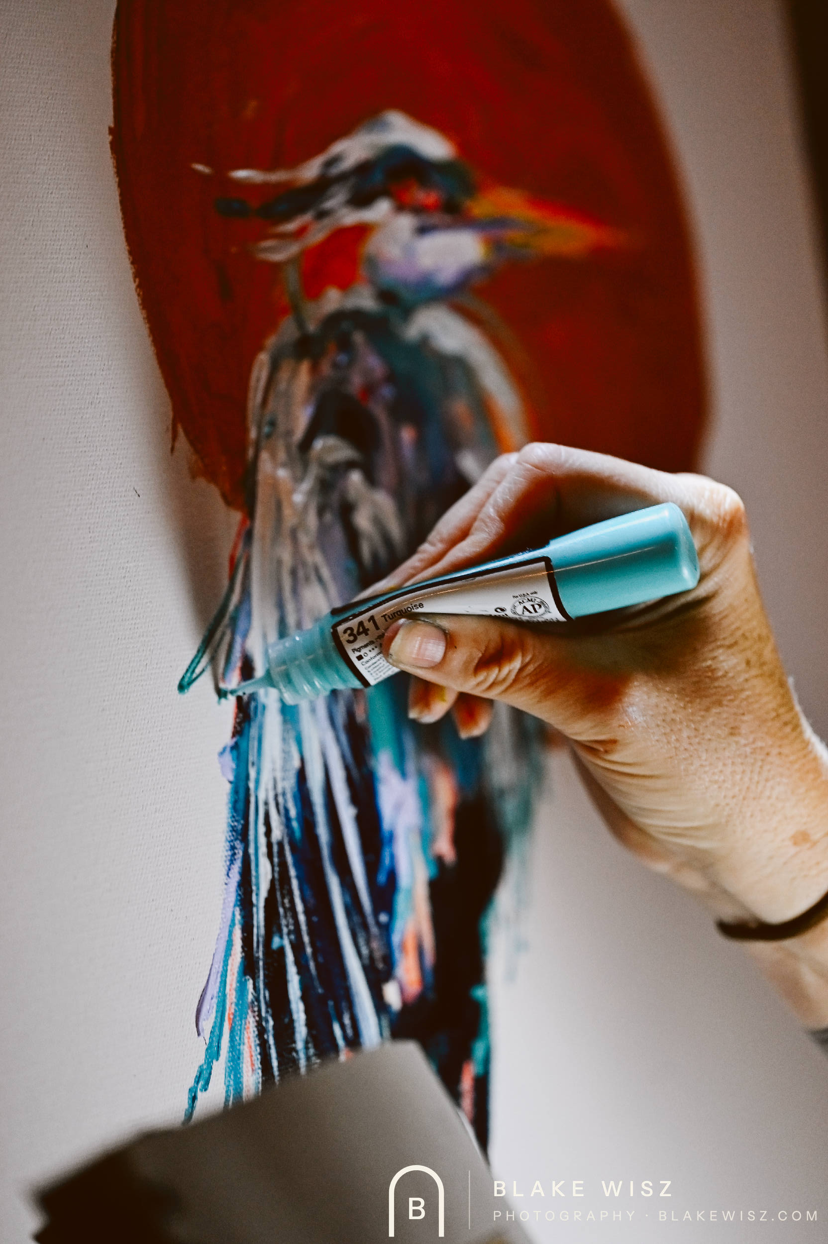 Close-up of a paint marker adding teal strokes to a heron canvas at Art Battle Ormond Beach