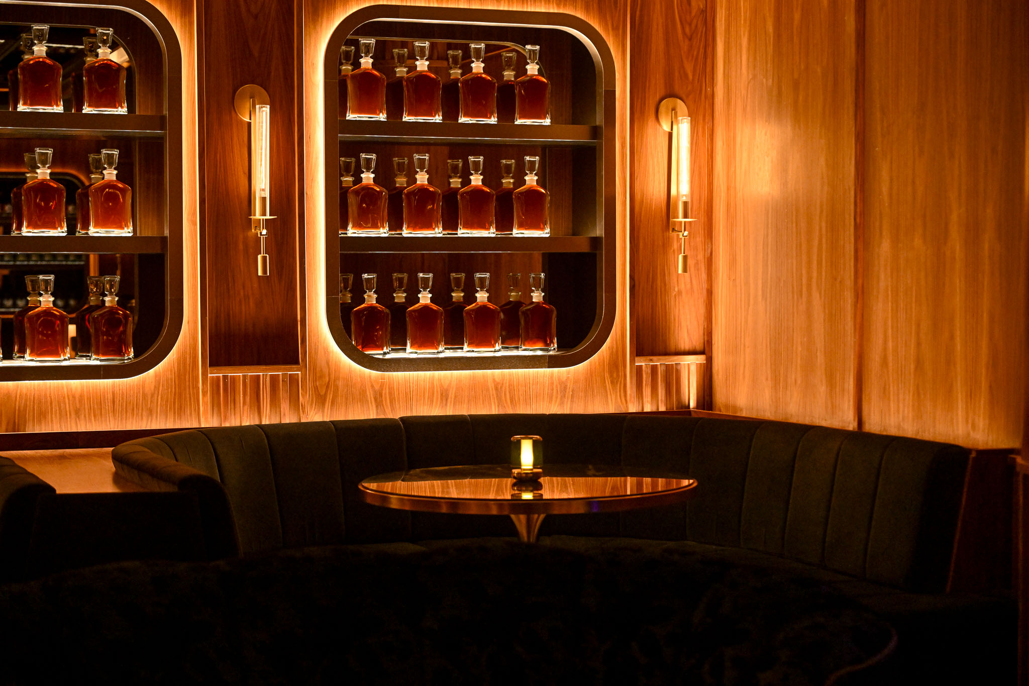 Backlit arched bottle displays above a curved leather banquette in the LucidWild bar