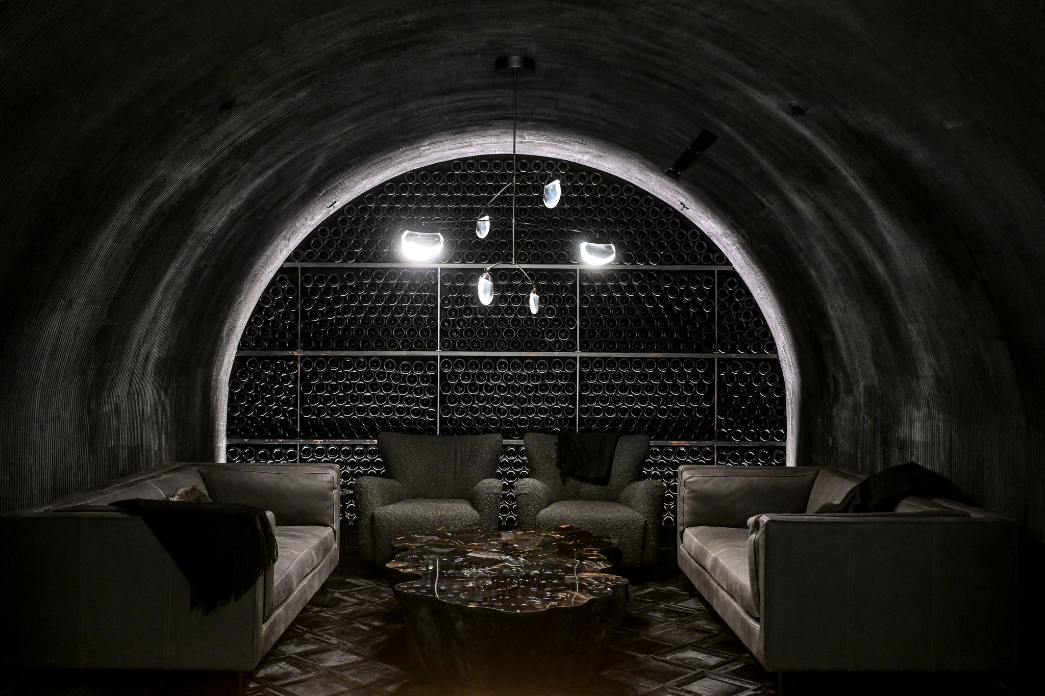Arched wall of racked wine bottles glowing inside the concrete cave lounge at LucidWild