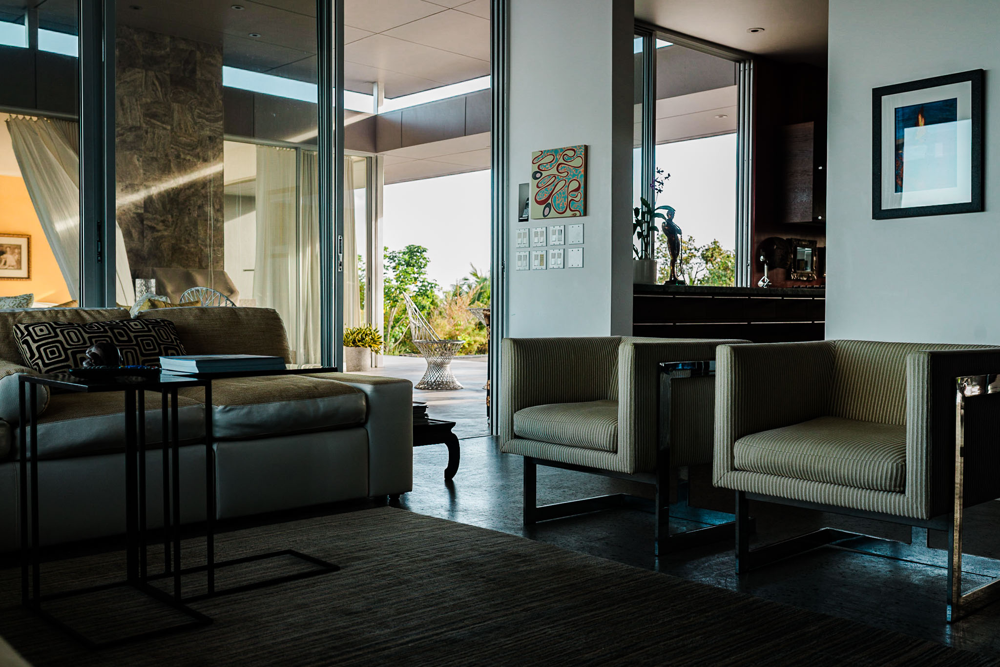 Sitting room with armchairs and a bench, glass opening to palms
