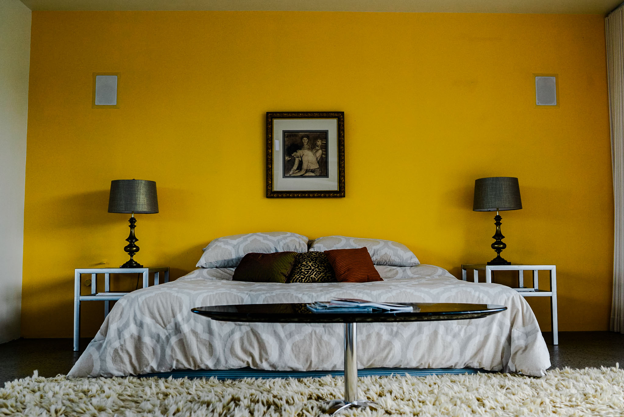 Bedroom with a yellow accent wall, framed art and matching bedside lamps