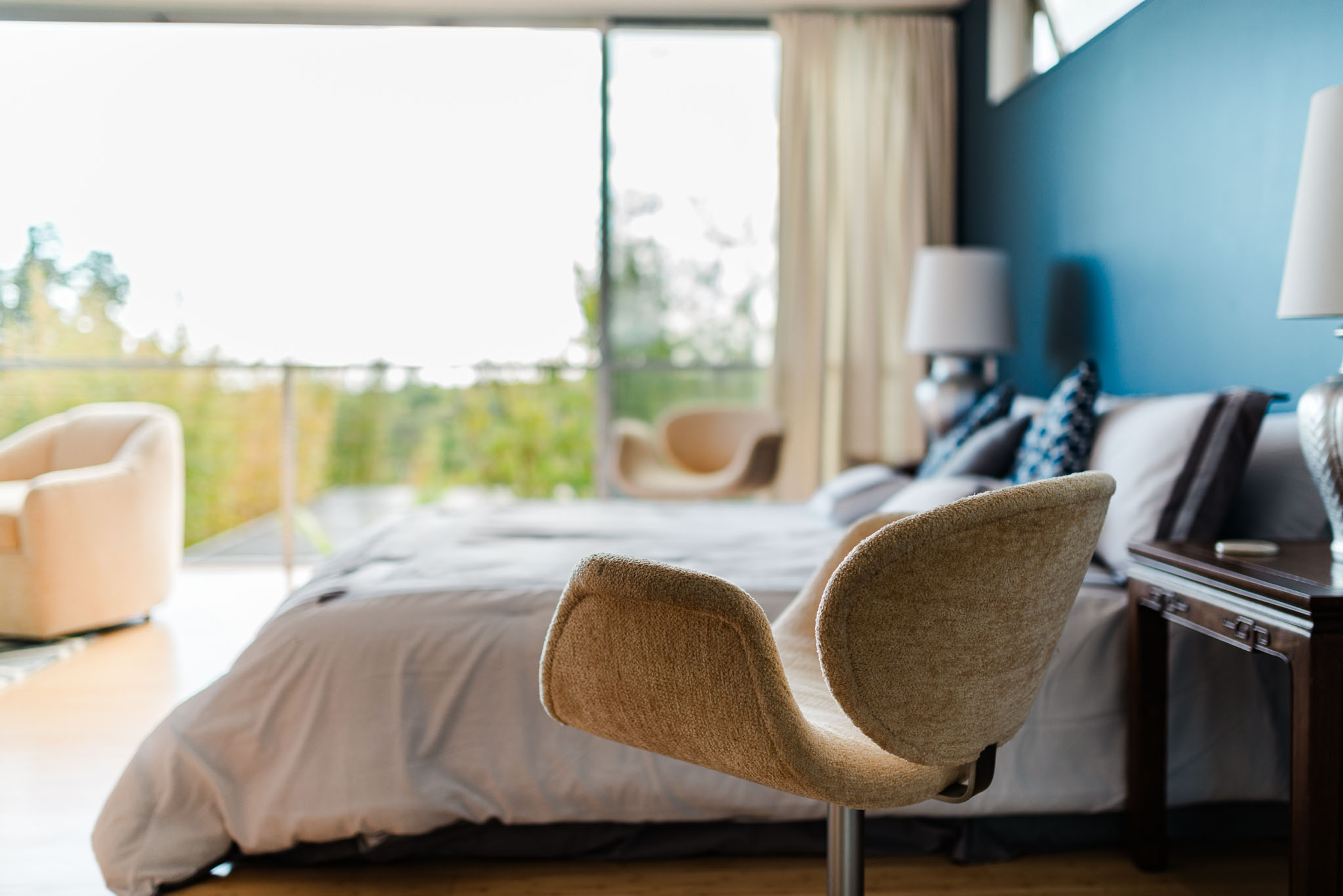 Sculptural woven chair at the foot of the bed against a blue wall