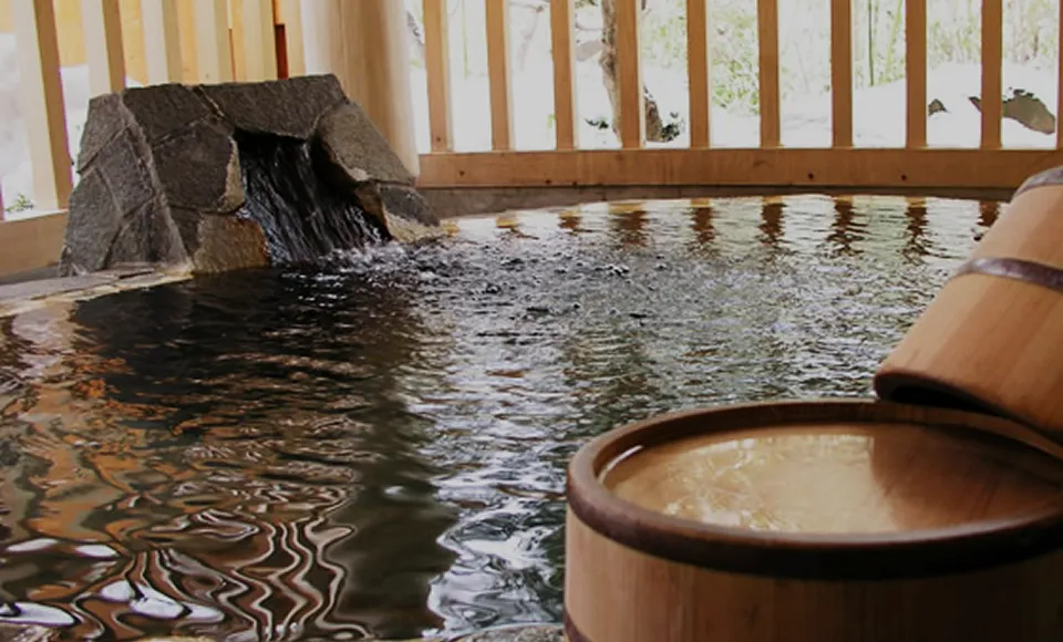 源泉が注がれる湯舟と木の桶。自然光が差し込む癒しの温泉空間