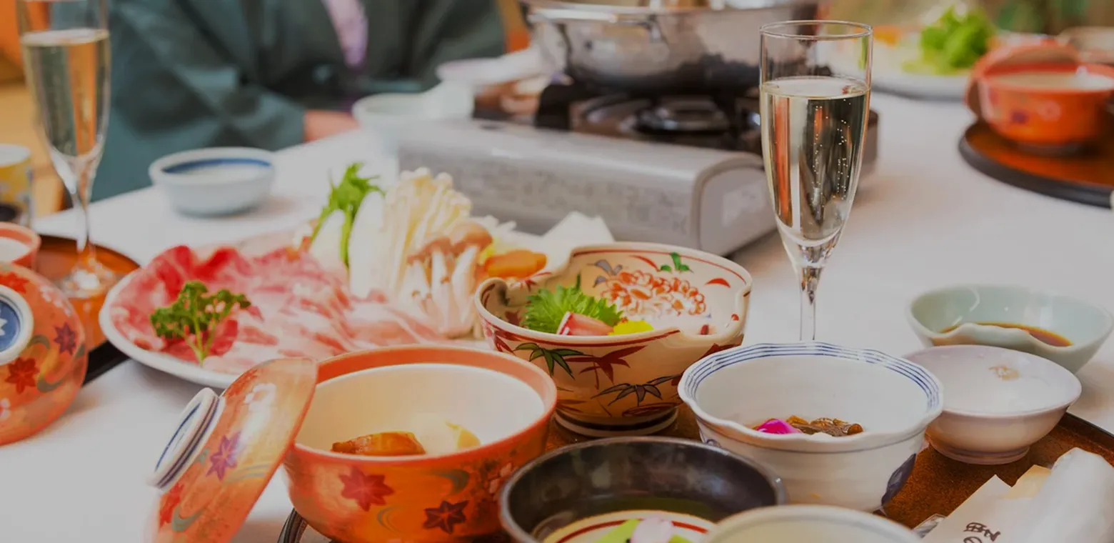 旅館の会席料理。小鍋、刺身、前菜の小鉢とともにスパークリングワインが添えられている