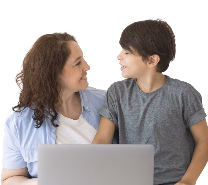 A woman and a young boy smiling at each other while sitting in front of a laptop.