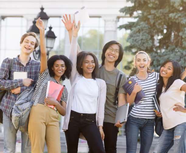 Group of six diverse college students standing outdoors with backpacks and notebooks, smiling and waving happily.