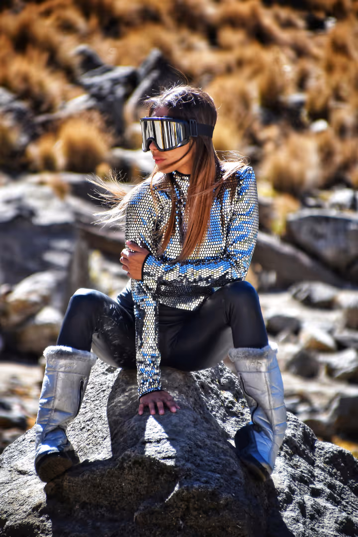 A woman in silver sits on rocks in the future like an ai tool that writes social media posts for me in my voice