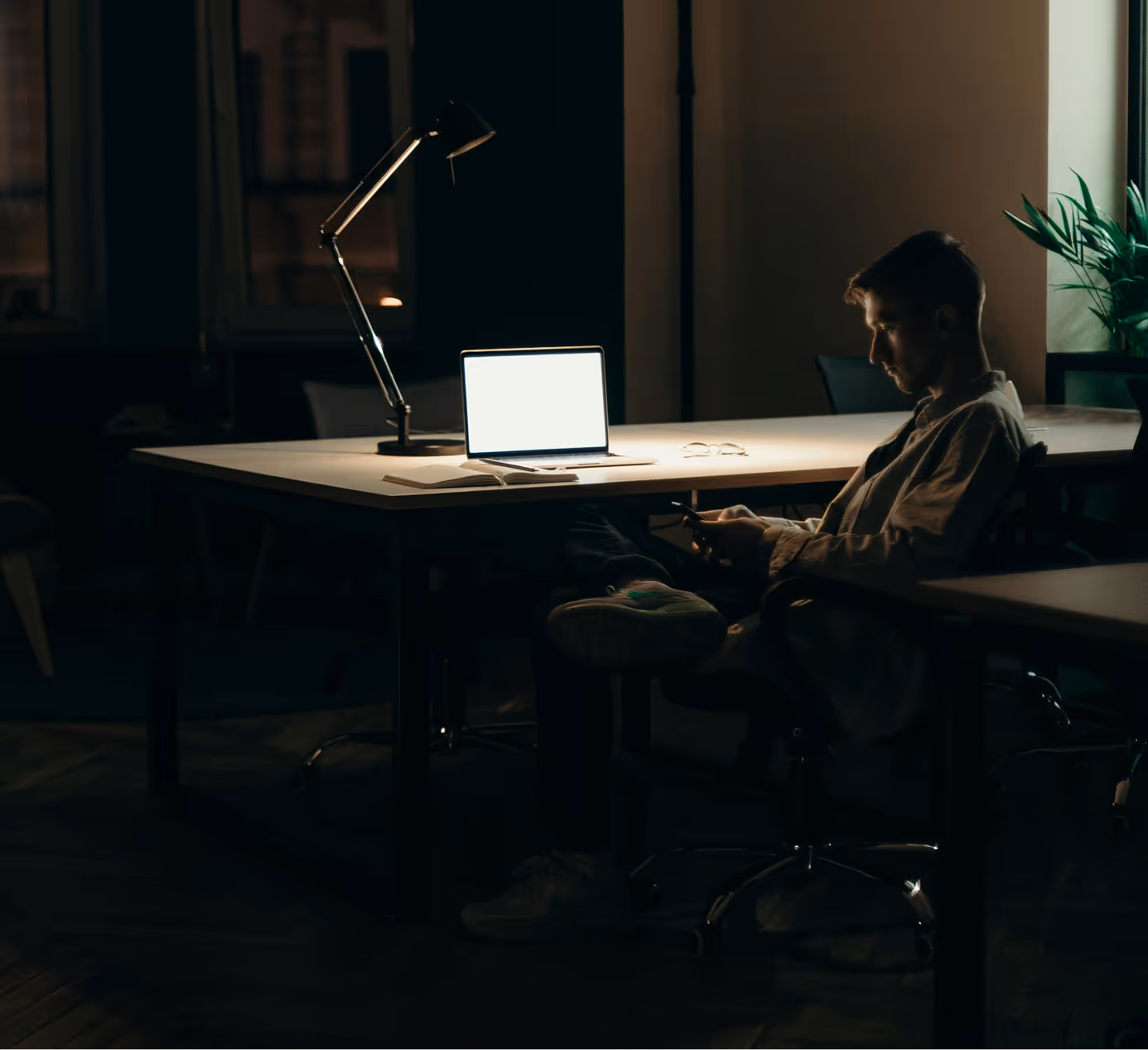 Guy at the office using smartphone in front of a laptop
