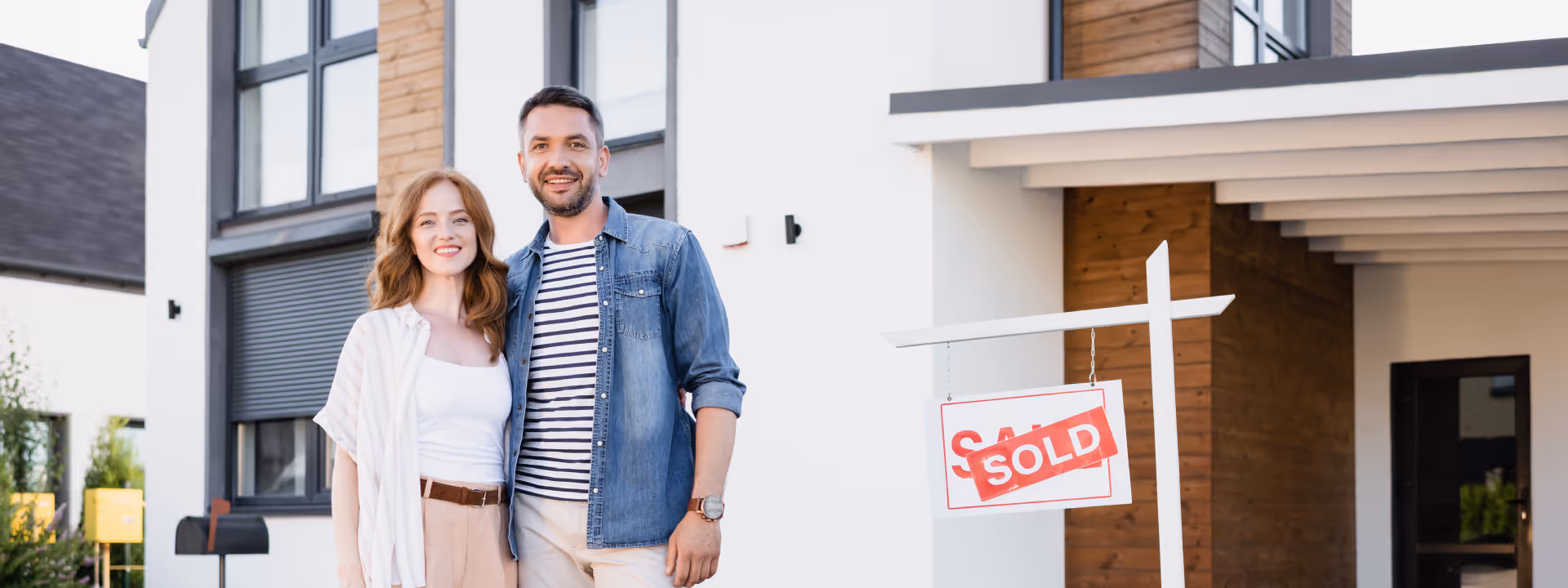 young couple standing outside house with sold sign