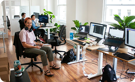 Image of developers smiling at the camera, in a cool, well lit co-working office.