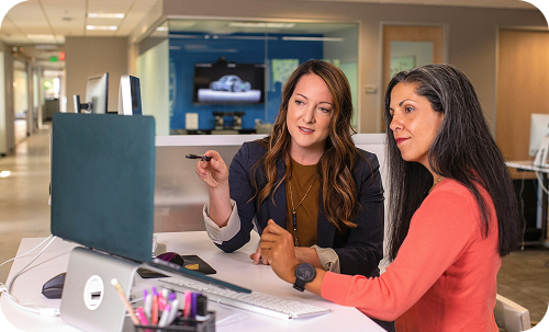 An image of two women talking and pointing through something on the computer.