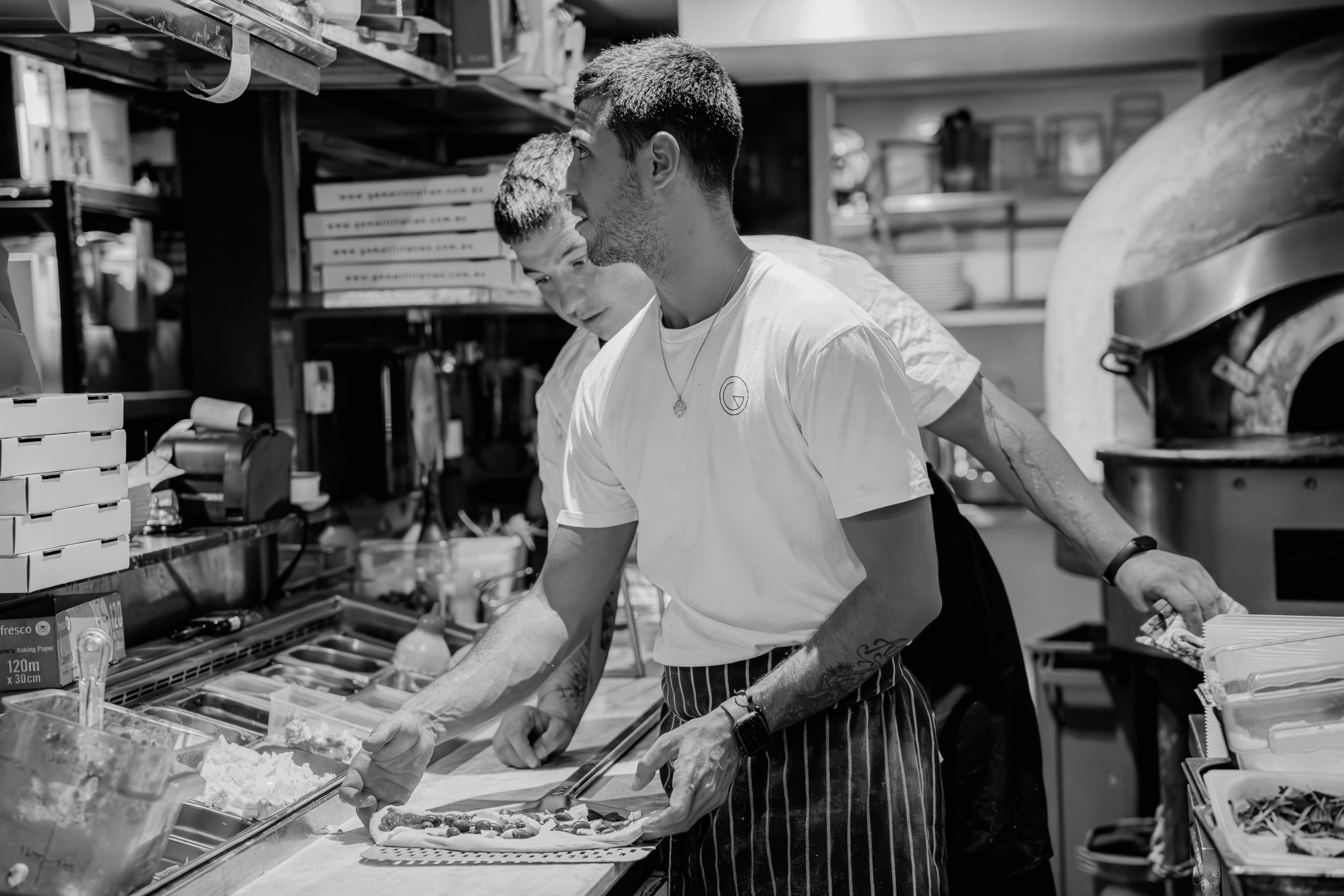 Two chefs in a kitchen prepare food, arranging ingredients on a counter.