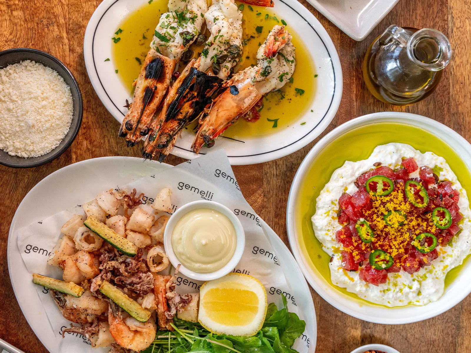 Three plates of food: grilled shrimp, fried seafood with lemon, and a creamy cheese dish with toppings.