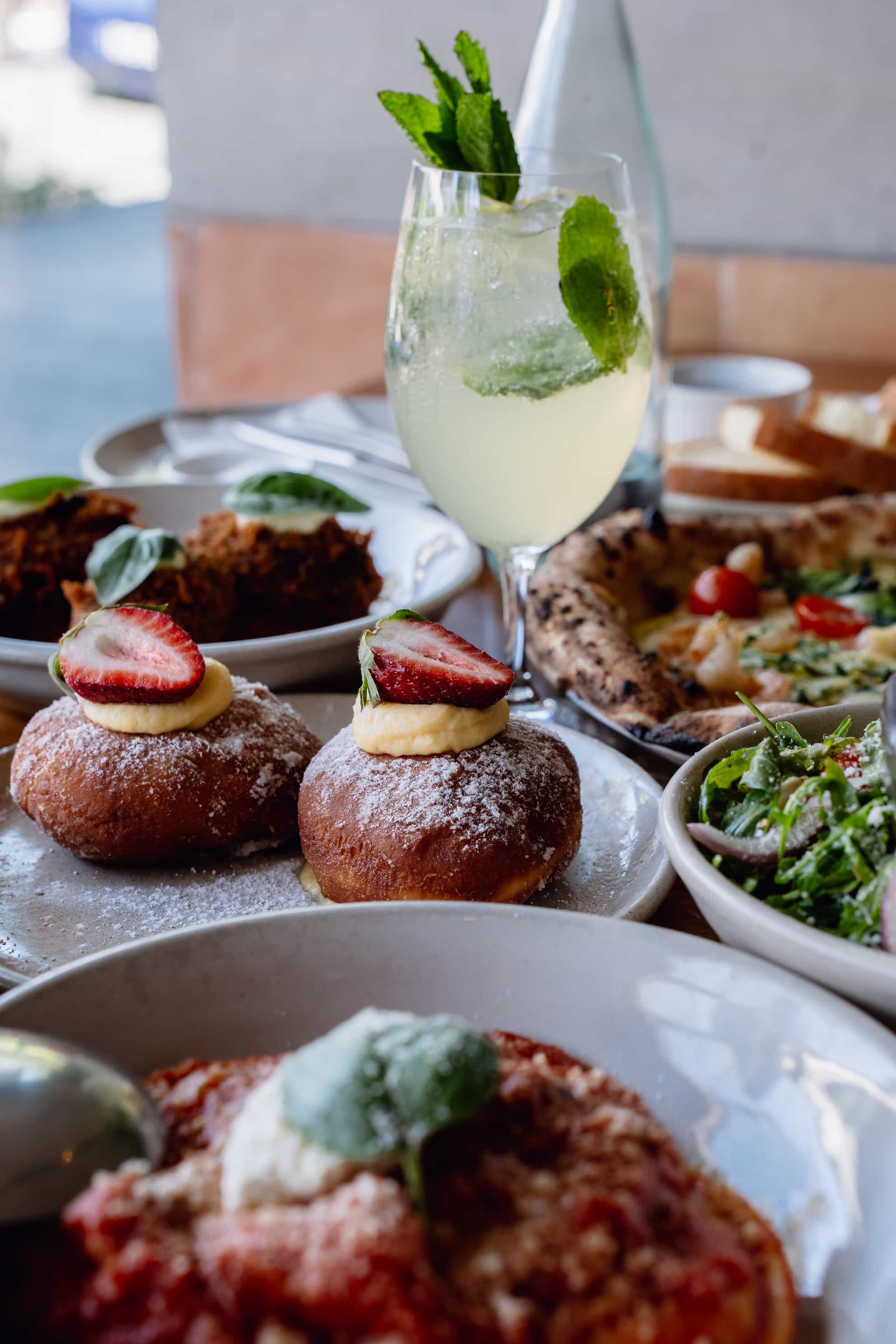 A table with various dishes, including strawberry-topped pastries and a glass of lemonade, is displayed.