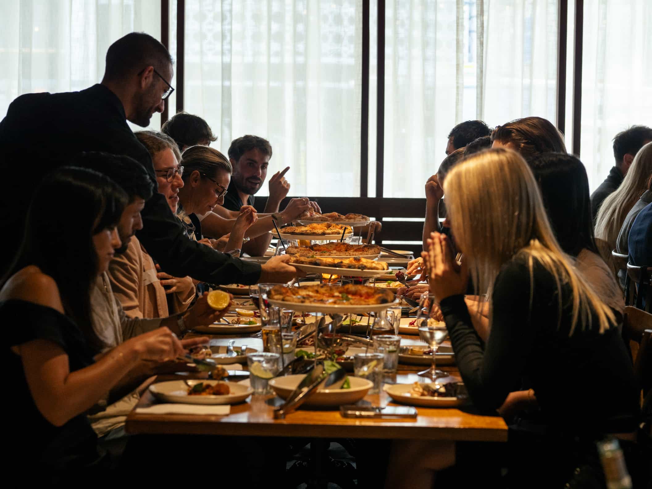 People seated at a long table enjoy a meal together in a restaurant setting.