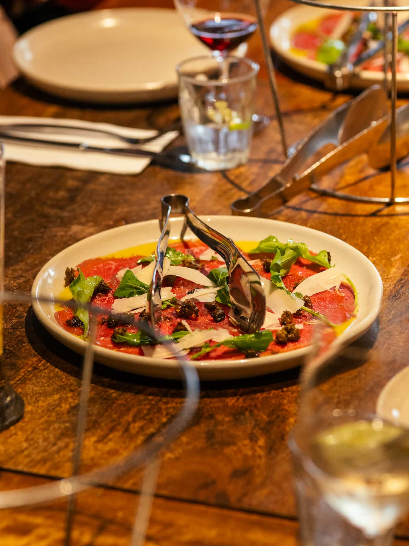 A plate of thinly sliced meat with greens and garnishes, served on a wooden table.