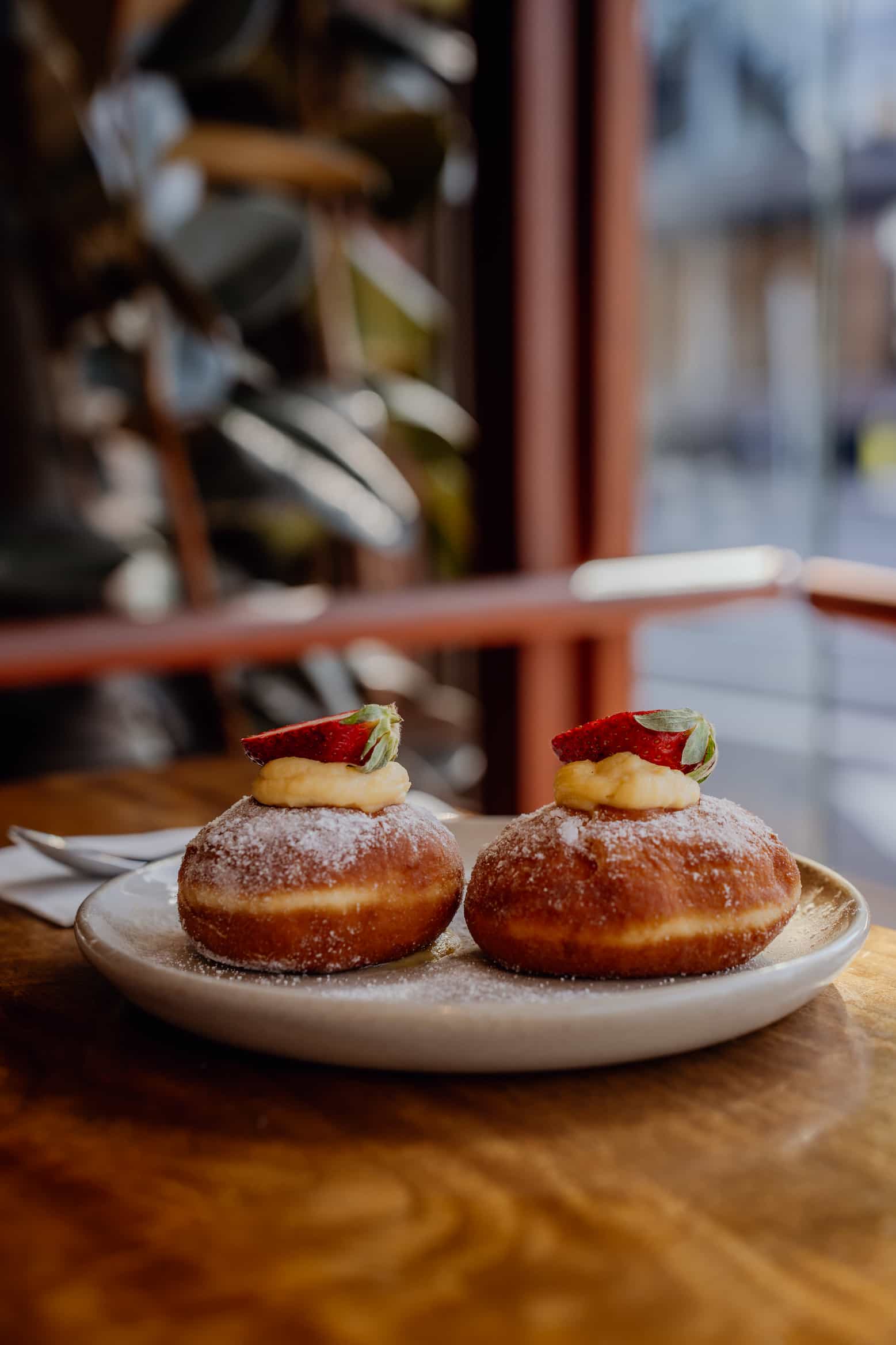 Two doughnuts on a plate topped with cream and strawberry slices.
