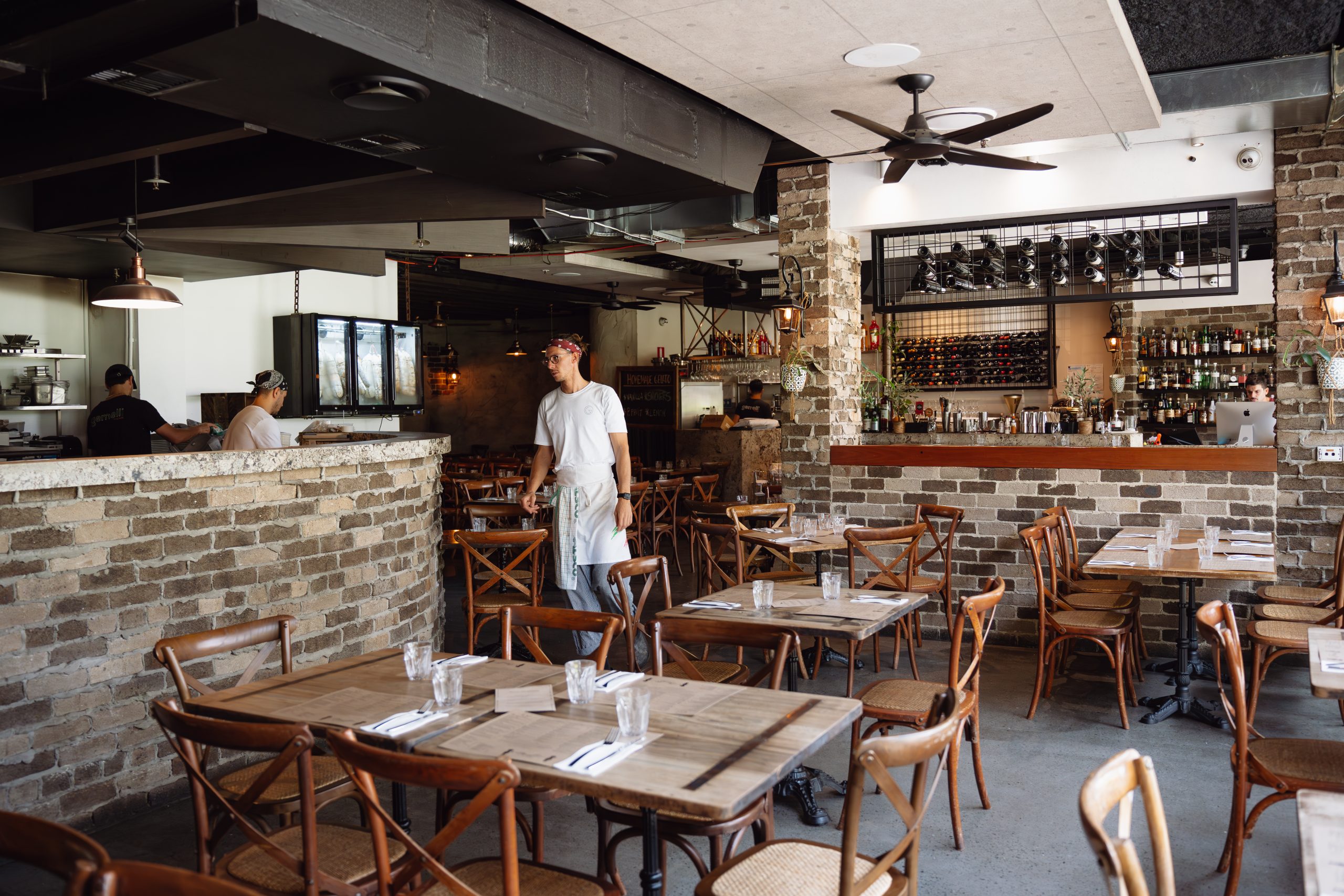 A restaurant worker cleans and sets tables in an empty dining area with rustic brick walls.