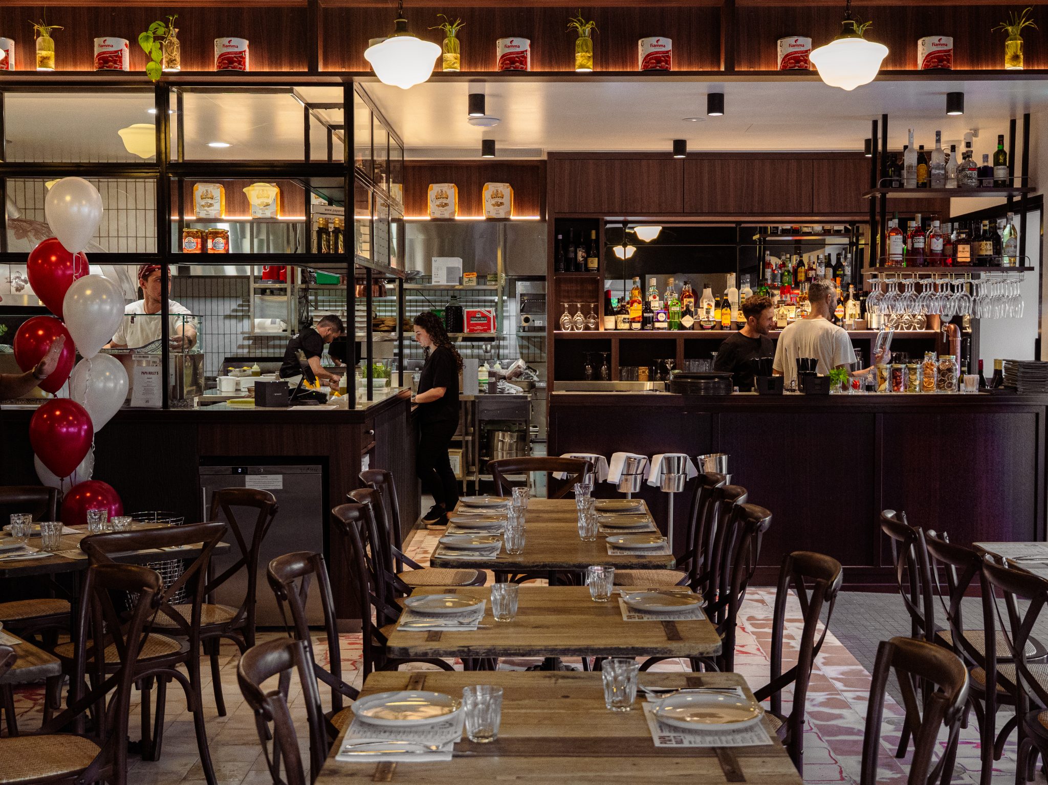 Restaurant interior with wooden tables set for dining; staff preparing behind the bar.