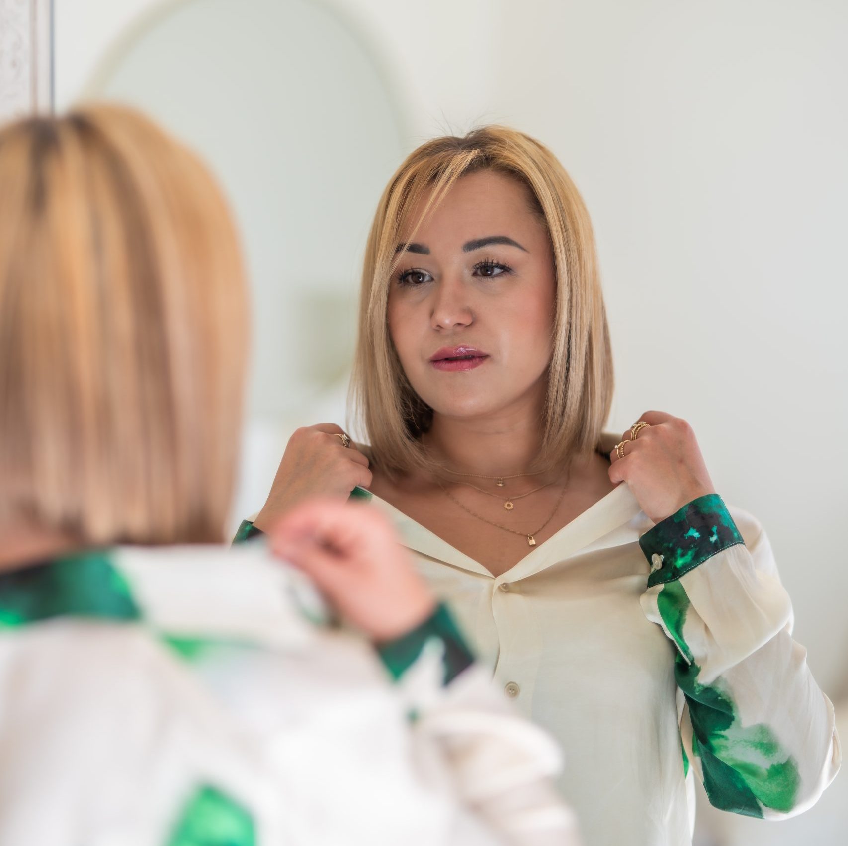 Samlyne, conseillère en image. Jeune femme de caract_re aux cheveux blonds qui place une chemise beige teintée de vert devant un miroir.