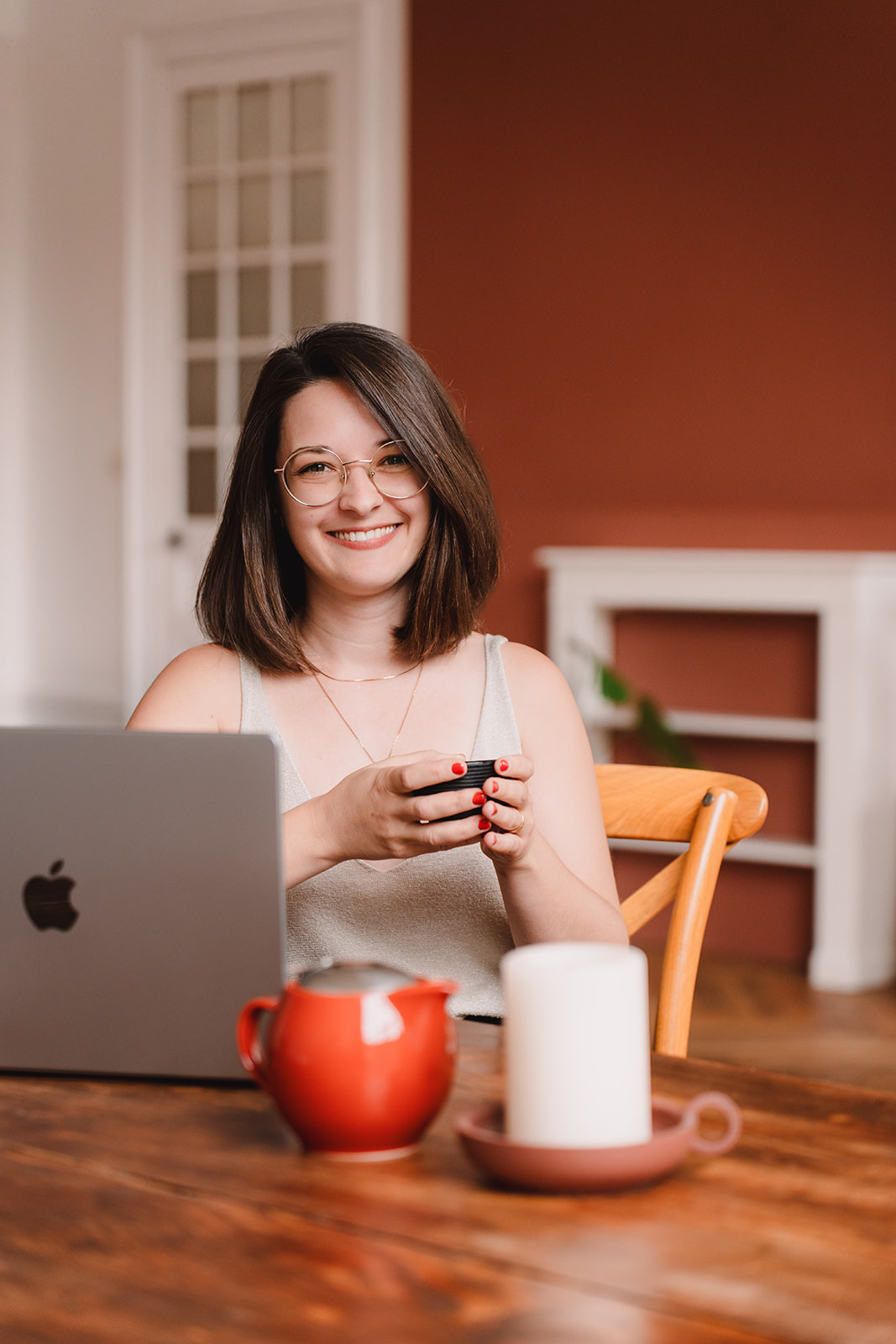 Line, femme de 30 ans aux cheveux châtains et aux lunettes arrondies, est assise une tasse à la main, la table devant elle montre son ordinateur ouvert, une théière et une petite bougie. Elle te regarde avec un sourire