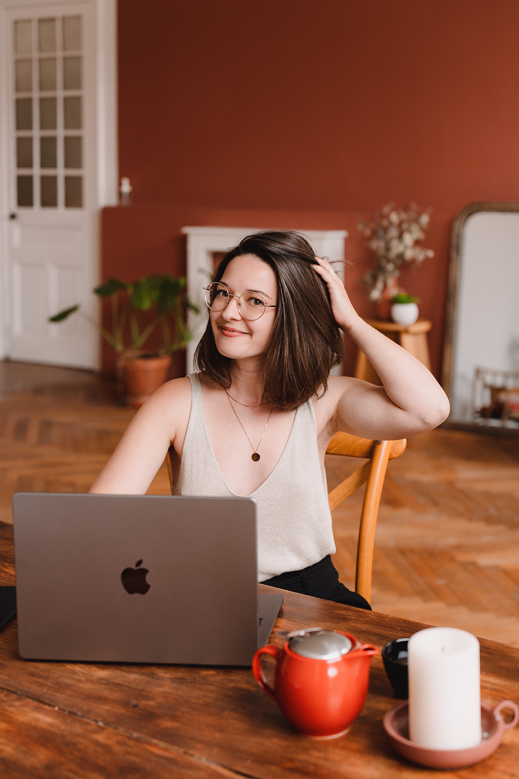 Line, jeune femme entrepreneure aux cheveux carrés châtains et aux lunettes arrondies, la tête inclinée vers toi un léger sourire, tient ses cheveux d'une main pour mieux te voir.