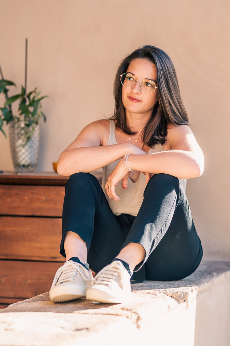 Line. Jeune femme entrepreneure assise sur un muret. Ses bras sont posés sur ses jambes repliées devant elle. Sa tête est tournée vers une personne qu'on ne voit pas. Elle l'écoute attentivement.