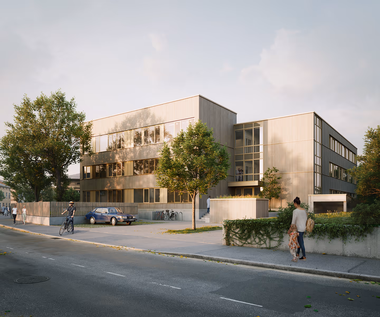 Modernes dreistöckiges Gebäude mit großen Fenstern, umgeben von Bäumen und Gehweg, mit Personen, die spazieren gehen und Fahrrad fahren.