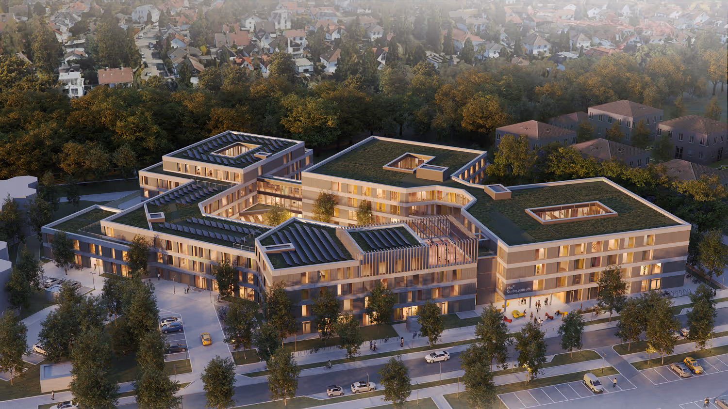 Luftaufnahme eines modernen Kinderzentrums mit begrünten Dächern, umgeben von Bäumen und Wohnhäusern im Hintergrund.